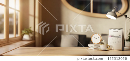 A clock atop books with coffee cup and calendar aside lamp on wooden table in a room with sunlight. 135312056