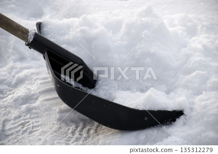 Close-up of a snow shovel digging into a pile of fresh, fluffy snow 135312279