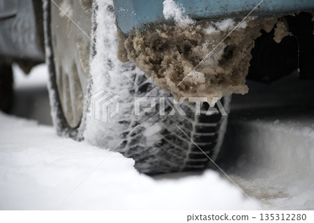 Snow-Covered Car Tire With Mud and Icicles on a Winter Road Scene 135312280