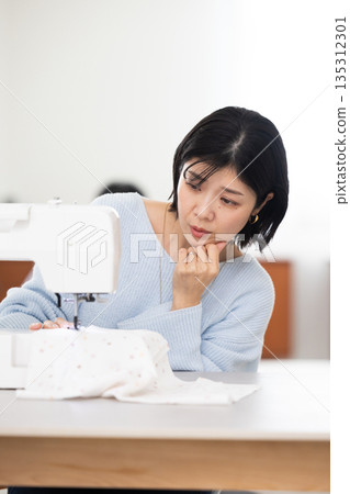 A middle-aged woman with a troubled expression while sewing A middle-aged woman with a troubled expression while sewing 135312301