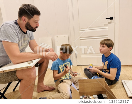 boys helping his father assemble a new piece of furniture with a screwdriver boys helping his father assemble a new piece of furniture with a screwdriver 135312517