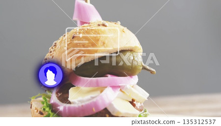 Showing stacked sandwich on wooden table with sesame bun, pickled onions, pepper spear and skewer 135312537