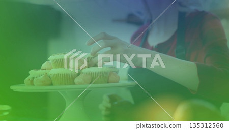 Placing woman in red top and apron arranging frosted cupcakes on cake stand on kitchen table Placing woman in red top and apron arranging frosted cupcakes on cake stand on kitchen table 135312560