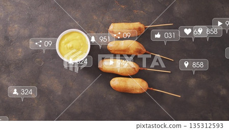 Displaying four corn dogs on wooden skewers on dark stone tabletop, with digital overlay icons 135312593