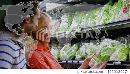 Selecting couple examining and choosing bagged lettuce in supermarket aisle, with world map overlay 135312637