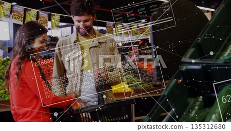Examining couple selecting produce from open bins in produce aisle with basket, digital panels 135312680