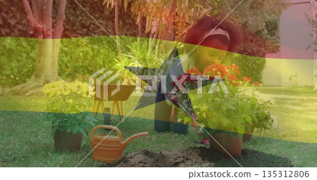 Kneeling child planting potted flowers on backyard lawn, with wheelbarrow, trowel and watering can 135312806