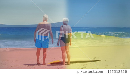 Standing senior couple gazing at ocean on sandy beach, with yellow bodyboard nearby Standing senior couple gazing at ocean on sandy beach, with yellow bodyboard nearby 135312836
