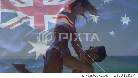 Man lifting partner overhead in swimwear on beach at shoreline, with fading Australian flag overlay Man lifting partner overhead in swimwear on beach at shoreline, with fading Australian flag overlay 135312837