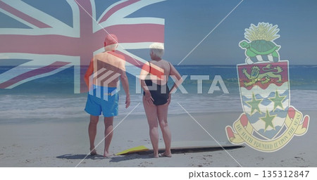 Gazing out senior couple standing on sandy shoreline, surfboard at feet with nautical flag overlay Gazing out senior couple standing on sandy shoreline, surfboard at feet with nautical flag overlay 135312847