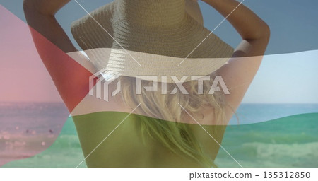 Standing woman wearing straw sun hat facing ocean on sandy beach, with red triangle flag overlay Standing woman wearing straw sun hat facing ocean on sandy beach, with red triangle flag overlay 135312850
