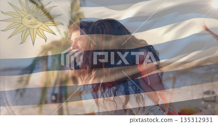 Couple riding piggyback on sandy beach with Uruguay flag overlay, palm trees and ocean water Couple riding piggyback on sandy beach with Uruguay flag overlay, palm trees and ocean water 135312931