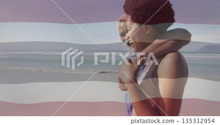 Embracing couple gazing toward horizon on sandy beach, with waves and pale blue sky, copy space 135312954