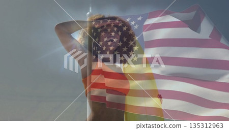 Standing woman wearing orange swim top under clear blue sky, with sun flare, American flag overlay 135312963