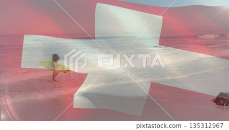 Standing woman surfer holding yellow surfboard in shallow surf at sandy beach, Swiss cross overlay 135312967