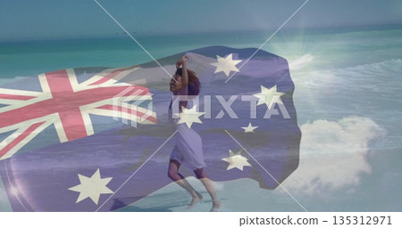 Running African woman wearing dress holding Australian flag in ocean waves on sandy beach, freedom 135312971