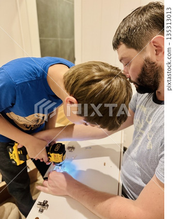 teen age boy helping his father assemble a new piece of furniture with a screwdriver teen age boy helping his father assemble a new piece of furniture with a screwdriver 135313013