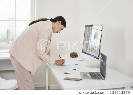 Businesswoman accountant auditing financial charts on desktop computer in office Businesswoman accountant auditing financial charts on desktop computer in office 135313279