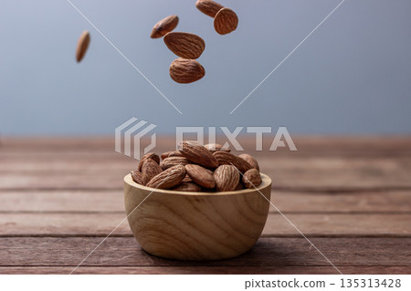 Almond snack fruit in wooden bowl, Falling almond seeds scattered all blurred background 135313428