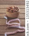 Almonds in a wooden cup on a wood plate with a measuring tape, symbolizing healthy diet control. 135313492