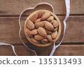 Almonds in a wooden cup on a wood plate with a measuring tape, symbolizing healthy diet control. 135313493