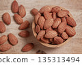 Almonds placed in a wooden cup and on a natural wood plate, highlighting simple organic textures. 135313494