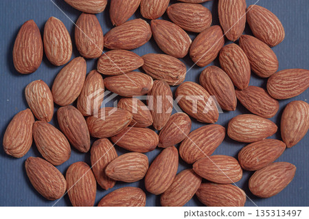 Almonds rest on a simple piece of paper, highlighting their natural texture in a clean minimal scene. 135313497