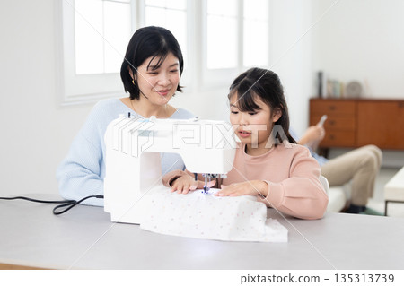 一個小學生女孩和她媽媽一起縫紉 135313739