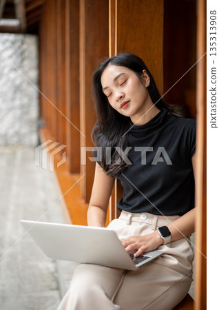 Asian woman holding laptop and sleeping or napping while sitting on wooden bench in a corridor or hallway of cafe. Asian woman holding laptop and sleeping or napping while sitting on wooden bench in a corridor or hallway of cafe. 135313908