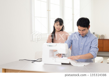 A father sewing next to his elementary school daughter 135314386