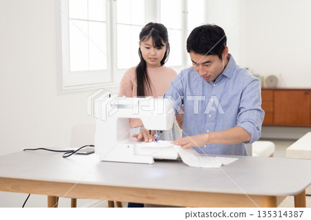 A father sewing next to his elementary school daughter A father sewing next to his elementary school daughter 135314387
