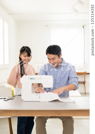 A father sewing next to his elementary school daughter 135314392