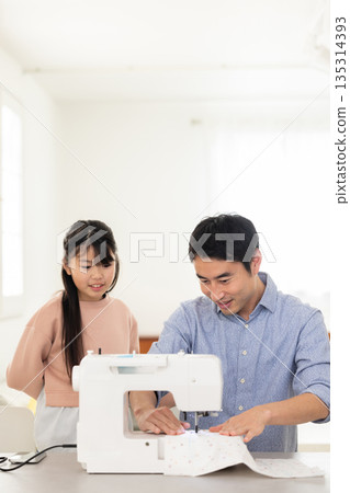 A father sewing next to his elementary school daughter 135314393