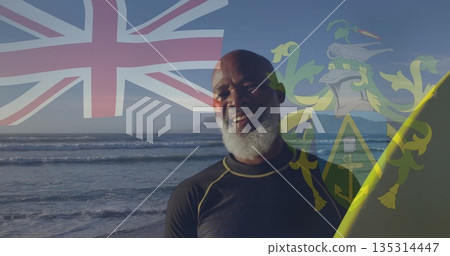 Standing surfer wearing black wetsuit on beach holding yellow board with Union Jack and crest flags Standing surfer wearing black wetsuit on beach holding yellow board with Union Jack and crest flags 135314447