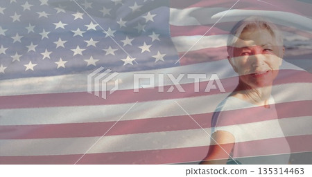 Smiling senior woman gazing toward ocean at sandy beach, with American flag overlay, copy space 135314463