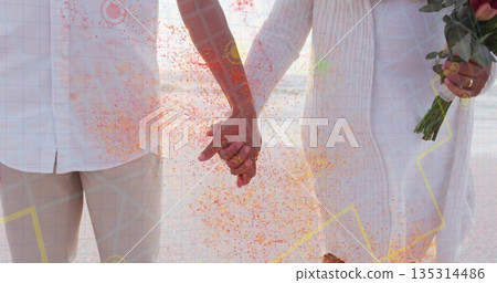 Holding hands senior couple wearing white linen in studio, with pink tulip bouquet, confetti, grid 135314486