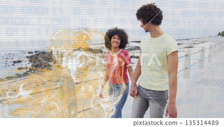 Walking couple holding hands along seaside promenade, with white railing and breaking ocean waves 135314489