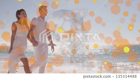 Walking couple wearing white linen shirt, sleeveless sundress along sandy shoreline in sunlight Walking couple wearing white linen shirt, sleeveless sundress along sandy shoreline in sunlight 135314498