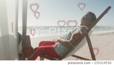 Reclining woman wearing red leggings, blue top on beach in deck chair, heart graphics, copy space 135314550