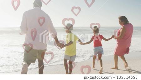 Walking family of four holding hands on wet sand at ocean edge, with straw fedora hat 135314553