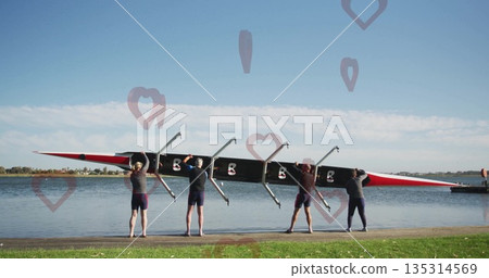 Four rowers wearing sports attire lifting racing shell on shoreline by dock, with riggers and oars 135314569