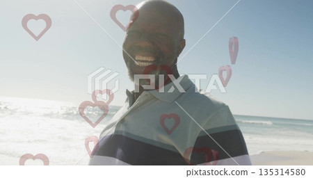 Smiling man wearing striped polo shirt standing on sandy beach shoreline, with heart overlay 135314580