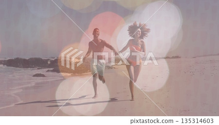 Running couple wearing orange bikini, trunks on sandy shore, with waves crashing on rocks Running couple wearing orange bikini, trunks on sandy shore, with waves crashing on rocks 135314603