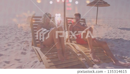 Couple wearing swimwear and sunglasses reclining on beach chairs under umbrella, holding cocktail 135314615
