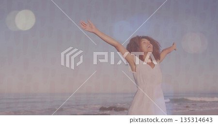Raising arms woman standing on sandy shoreline, with gentle surf and pastel sunrise sky 135314643