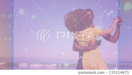 Dancing couple embracing on sandy beach under pastel sky, with gentle waves rolling 135314673