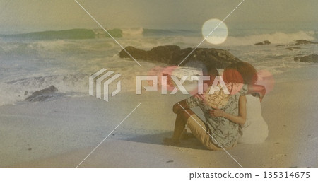 Sitting couple wearing tropical shirt and sundress hugging on sandy beach, with ocean waves 135314675