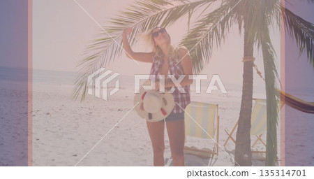 Standing woman holding inflatable ring on beach under palm tree with sunglasses and hammock 135314701