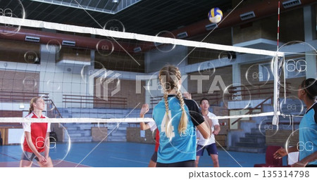 Teen volleyball player spiking ball over net in sports hall, wearing blue-black jersey, 6G overlays Teen volleyball player spiking ball over net in sports hall, wearing blue-black jersey, 6G overlays 135314798