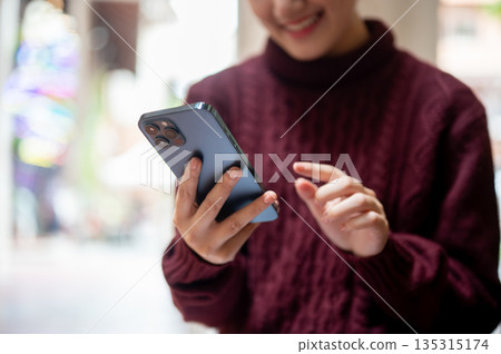 Close up of woman hand holding and fingers pointing at smartphone while sits or stands in a building 135315174